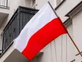 Flaga Polski w pionie, biało-czerwona, powiewa na tle budynku z balkonem.