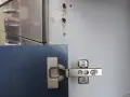 Cerniera di un mobile blu fissata con viti. Vicino, un foro nel legno indica come avvitare una vite che gira a vuoto nel legno.