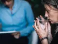 Kobieta pije wodę z kieliszka, siedząc naprzeciwko terapeuty.