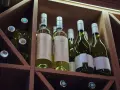 Butelki białego wina w drewnianym regale. Zastanawiasz się, czy szampan może się przeterminować? Te butelki czekają na degustację.
