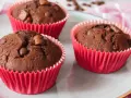 Drei saftige Schokomuffins mit Schokostückchen in roten Papierförmchen, perfekt für Kinder.