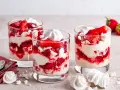 Drei Gläser mit Eton Mess: geschichtete Erdbeeren, Sahne und zerbrochene Baiser-Stücke.