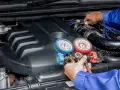 Mecánico realiza carga de gas al aire acondicionado de un coche, usando manómetros para verificar la presión.