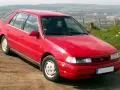 Czerwony Hyundai Pony z lat 90. stoi na polnej drodze, z widokiem na dolinę i miasto w tle.