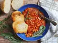Fagioli all'uccelletto in umido con pomodoro, serviti con pane tostato e erbe aromatiche. Perfetti per scoprire cosa abbinare ai fagioli all'uccelletto.