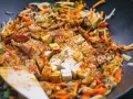 Kawałki tofu i kolorowe warzywa po chińsku smażą się na patelni wok, przyprawione kurkumą i papryką.