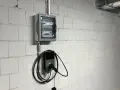 Nowoczesne gniazdo do ładowania samochodu elektrycznego Autel zamontowane na białej, ceglanej ścianie obok skrzynki z bezpiecznikami.