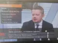 Mężczyzna w garniturze na ekranie telewizora, na którym widać menu z opcją "477 - TV Trwam".