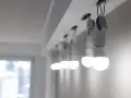 Rząd białych żarówek LED, wiszących na przewodach, świeci jasno, mimo że instalacja wygląda na nieukończoną.