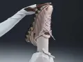 Różowy but Nike na obcasie, trzymany przez dłoń w białej rękawiczce.