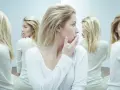 Kobieta z blond włosami w białej bluzce, otoczona swoimi odbiciami w lustrze.