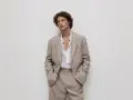 Uomo con capelli ricci indossa un completo beige, incarnando l'eleganza discreta dell'old money significato.