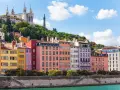 Colorful buildings line the river in Lyon, France, with a basilica on the hill above. A perfect scene for Lyon travel.