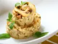 Kremowe risotto z grzybami, udekorowane listkami bazylii i oregano, prezentuje się apetycznie na białym talerzu.