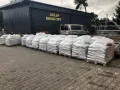 Palety z workami materiałów budowlanych przed sklepem drogowym.