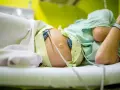 Kobieta w ciąży leży na łóżku, podłączona do aparatury KTG. Widać jej brzuch z przyczepionymi czujnikami.