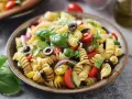 Un'insalata di pasta fredda sfiziosa con fusilli, pomodorini, olive nere, cetrioli, cipolla rossa e basilico fresco.