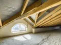 Poddasze w trakcie budowy, widoczne drewniane krokwie o kącie nachylenia dachu 30 stopni, okno łukowe i betonowa podłoga.