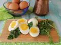 Uova sode in friggitrice ad aria, tagliate a metà, su tagliere con rucola e prezzemolo. Un modo sano e veloce per preparare le uova.
