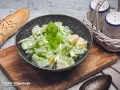 Ein cremiger sellerie salat mit frischem Basilikum, serviert in einer Schale neben einem Baguette und Salz- und Pfefferstreuern.