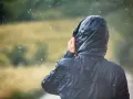 Person im Regen, die Kapuze einer Jacke mit PU-Beschichtung festhält.