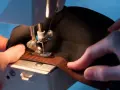 Mains habiles guidant un tissu noir sous une machine à coudre pour coudre du velcro marron.