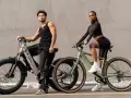 A man and woman pose with their electric bikes. This shows what a hybrid bike is good for: versatile riding on various terrains, blending comfort and performance for urban commutes or light trails.