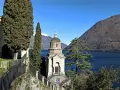 Un suggestivo lago con una piccola chiesa in mezzo, incorniciata da cipressi e montagne innevate.