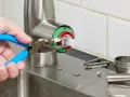 A hand uses pliers to remove a faucet cartridge, a key step in learning how to replace faucet cartridge.