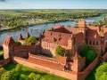 Malbork zamek krzyżacki, potężna twierdza z cegły, góruje nad rzeką Nogat. Otoczony murami, z wieżami i dziedzińcami, zaprasza do odkrywania historii.