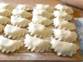 Surowe pierogi ułożone rzędami na drewnianej desce, posypanej mąką.