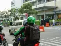 Zwei Personen auf einem Roller, der Fahrer trägt einen grünen Helm mit dem "Grab" Logo. Sie sind unterwegs in Thailand, um mit der Grab App Kunden zu transportieren.