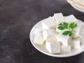 Queso paneer cortado en cubos en un plato blanco con una ramita de cilantro.