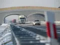 Autostrada A2 z mostem nad jezdnią, jadące samochody i ciężarówki w zimowej scenerii.