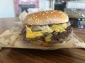 Podwójny cheeseburger z roztopionym serem, piklami i cebulą na bułce z sezamem.
