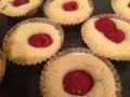 Flera glutenfria hallongrottor i pappersformar, med en hallon i mitten av varje.