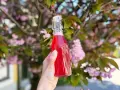 En hand håller en flaska med rosa rabarbersirap framför en blommande körsbärsträd.