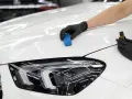 En hand med svart handske applicerar en skyddande beläggning på en vit bil för en djup, spegelblank finish.
