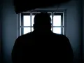Sylwetka mężczyzny wpatrująca się w okratowane okno. Czekam na dzień, gdy dozór policyjny kiedy się kończy i zobaczę wolność.