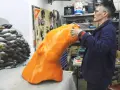 Artist applies finishing touches to a large, orange, 3D printed object, part of a project creating large objects.