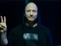 Wojtek Urbański w czarnej bluzie z kapturem pokazuje znak pokoju.
