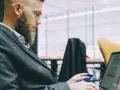 Hombre con barba y traje usa tarjeta de crédito en portátil. Busca cuánto se paga la hora extra en España.