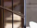 Dettaglio di un vetro con montanti scuri, riflessi tenui e polvere che si posa, creando un effetto quasi artistico.