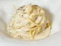 Un piatto di spaghetti cremosi, conditi con un'abbondante dose di cacio e pepe, cosparsi di pepe nero macinato.