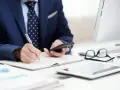 Biznesmen notuje, analizując dane. Rozważa przedawnienie kosztów komorniczych, trzymając telefon.