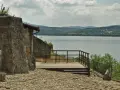 Kamienna wieża i drewniany taras z widokiem na spokojne jezioro dobczyckie. W oddali zalesione wzgórza.