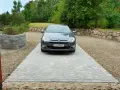 Grå bil parkerad på en vacker stenlagd uppfart. En fin uppfart inspiration med stenmur och grönska i bakgrunden.