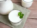Un pichet et deux verres de lait fermenté, l'un garni de menthe fraîche. Une liste des yaourts fermentés à déguster.