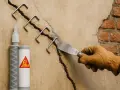 Réparation d'un enduit fissure extérieur avec des agrafes métalliques et un produit Sika. Un artisan applique le mortier.