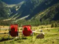 Dwie osoby w czerwonych leżakach podziwiają widok na Alpy w Austrii. Idealne miejsce na camping.